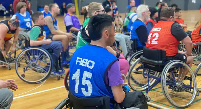 Group of wheelchair basketballers surrounding one another in different coloured sports bibs.