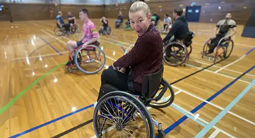 Ivana is a 25 year old young blonde woman strutting her chair on the basketball court. Enable New Zealand sticker is on the side.